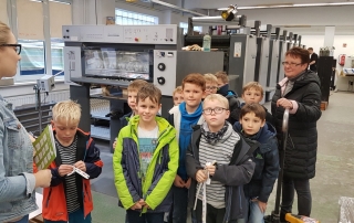 Kindergruppe mit Lehrerin besichtigt eine Druckmaschine in moderner Produktionshalle