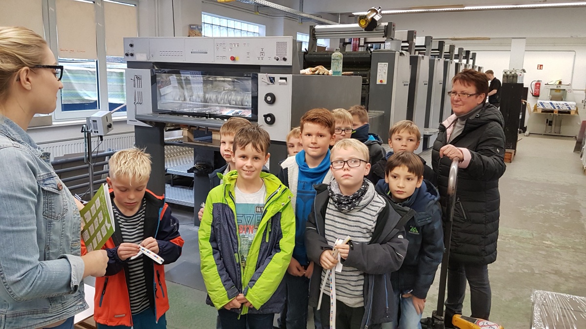 Kindergruppe mit Lehrerin besichtigt eine Druckmaschine in moderner Produktionshalle