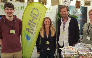 Vier Personen am Messestand der MHD Druckerei, mit Roll-Up und bunten Flyern im Vordergrund
