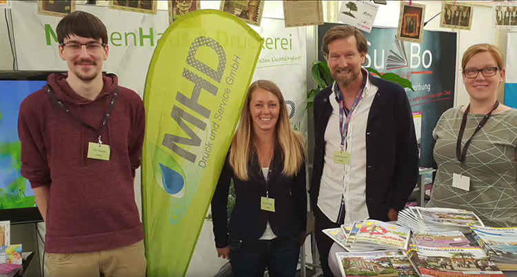 Vier Personen am Messestand der MHD Druckerei, mit Roll-Up und bunten Flyern im Vordergrund