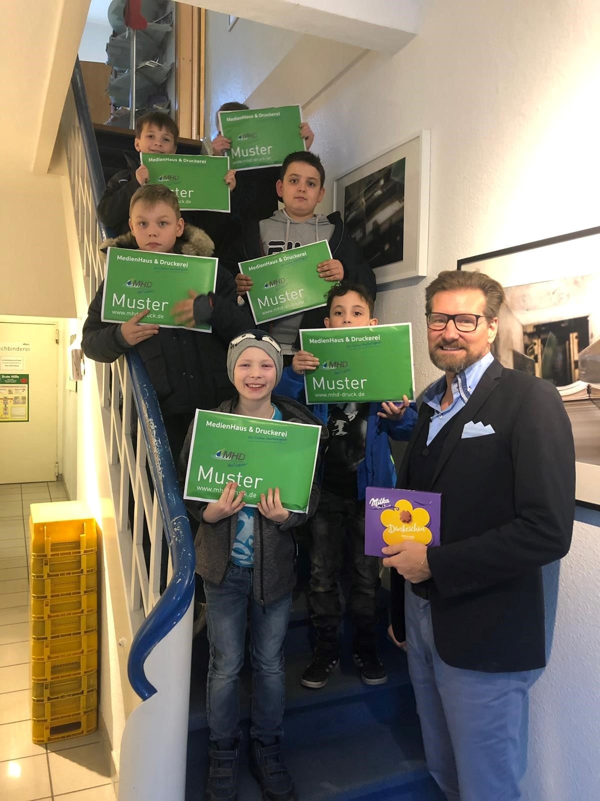 Kinder mit grünen MHD-Schildern auf Treppe, Mann hält Schokolade als Dank