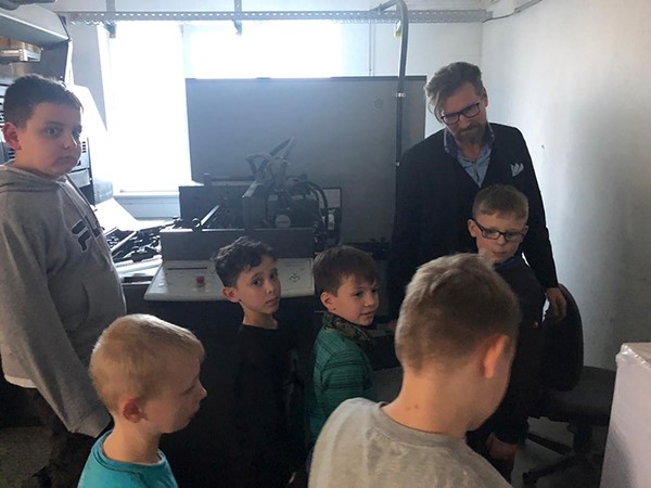 Kindergruppe steht mit einem Mann vor einer Maschine im dunkleren Raum