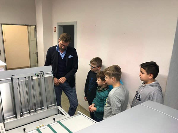 Mann erklärt Kindern eine Plattenbelichtungsmaschine in einem Raum der Druckerei
