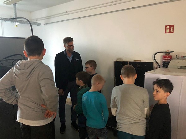 Kindergruppe mit Mann bei Druckereiführung in einem Maschinenraum