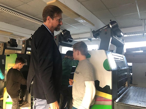 Kinder erkunden Druckmaschinen, Mann begleitet sie durch Produktionsraum