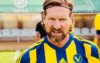 MHD Geschäftsführer als Fußballspieler im gelb-blauen Trikot mit Stirnband auf dem Spielfeld