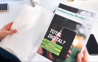 Person hält Magazin mit dem Titel „TOTAL DIGITAL?“ der Lutherischen Kirche