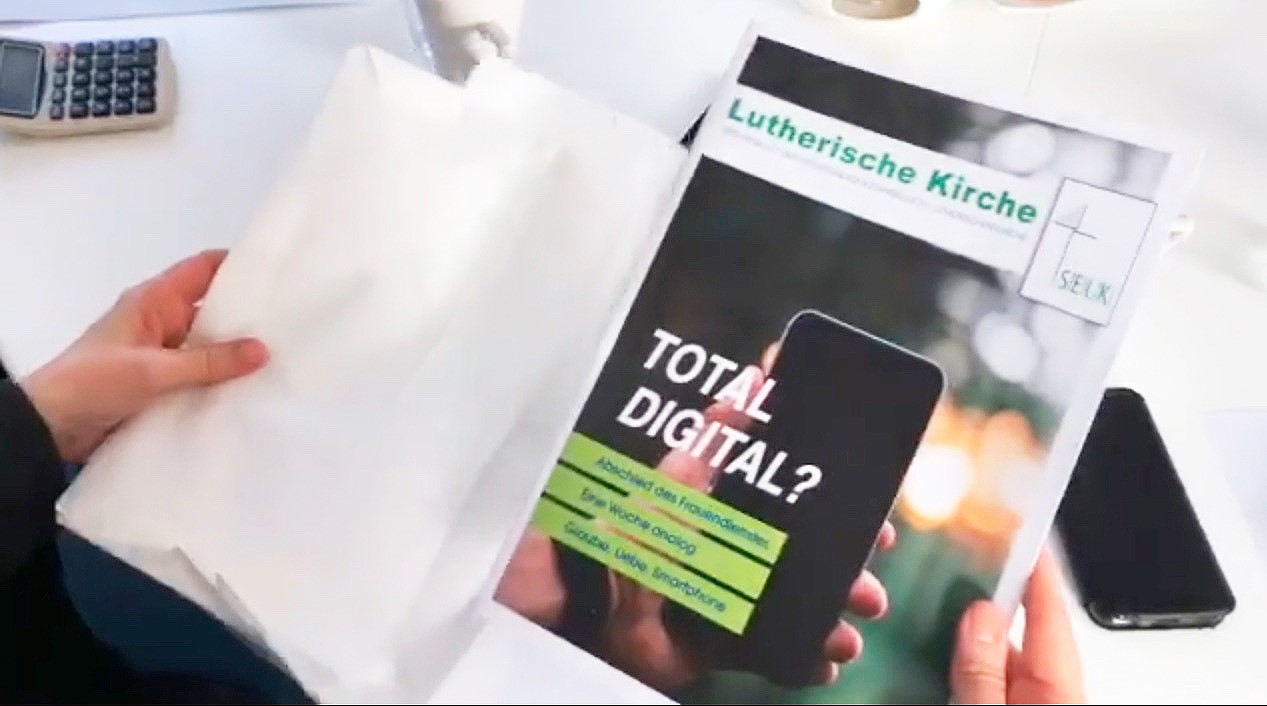 Person hält Magazin mit dem Titel „TOTAL DIGITAL?“ der Lutherischen Kirche