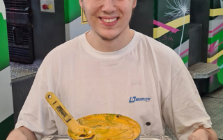 Junger Mann mit Druckfarbe in Dose auf Tablett vor bunter Offsetdruckmaschine