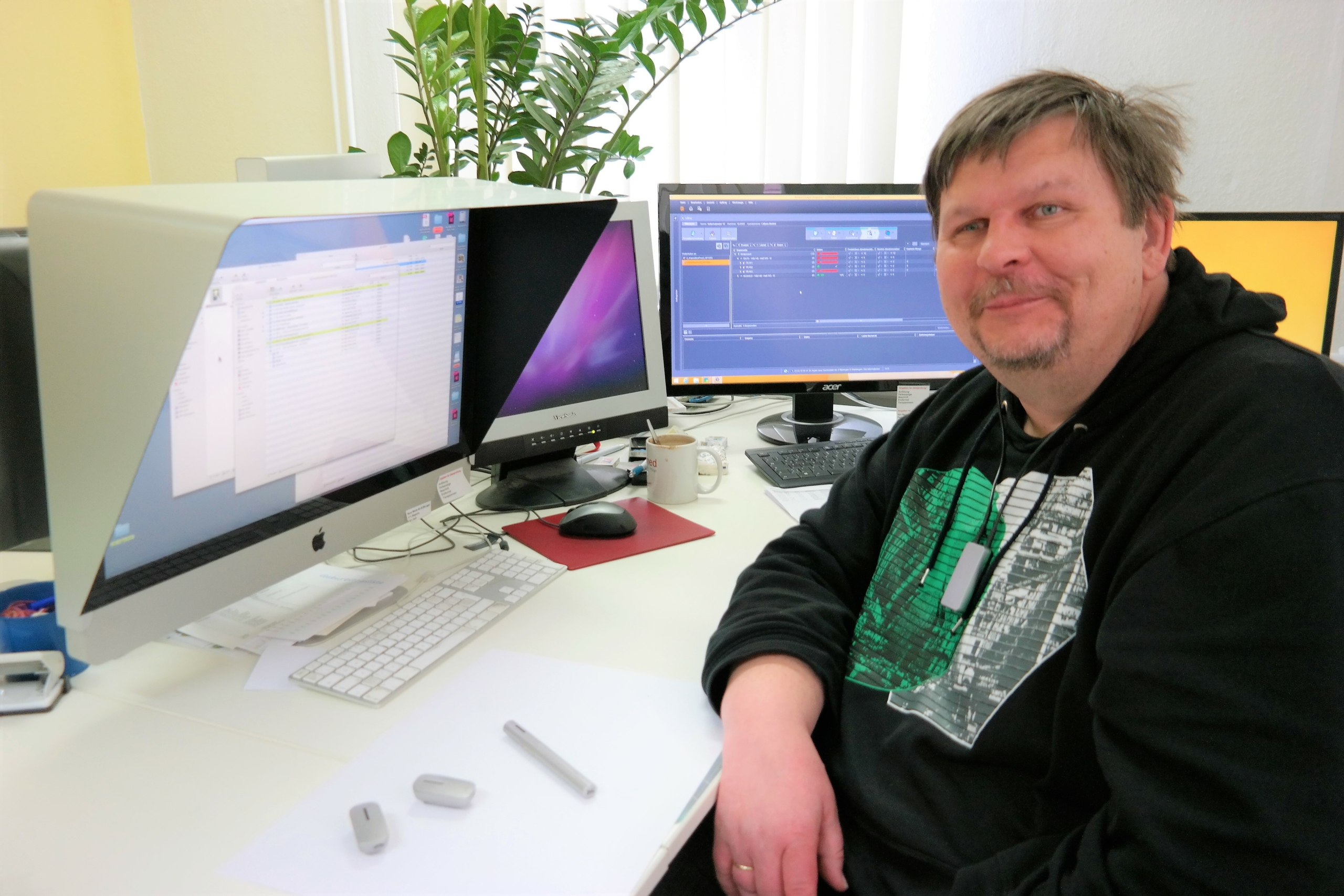 Mediengestalter am Arbeitsplatz: Mann im schwarzen Hoodie sitzt vor Monitoren im modernen Büro