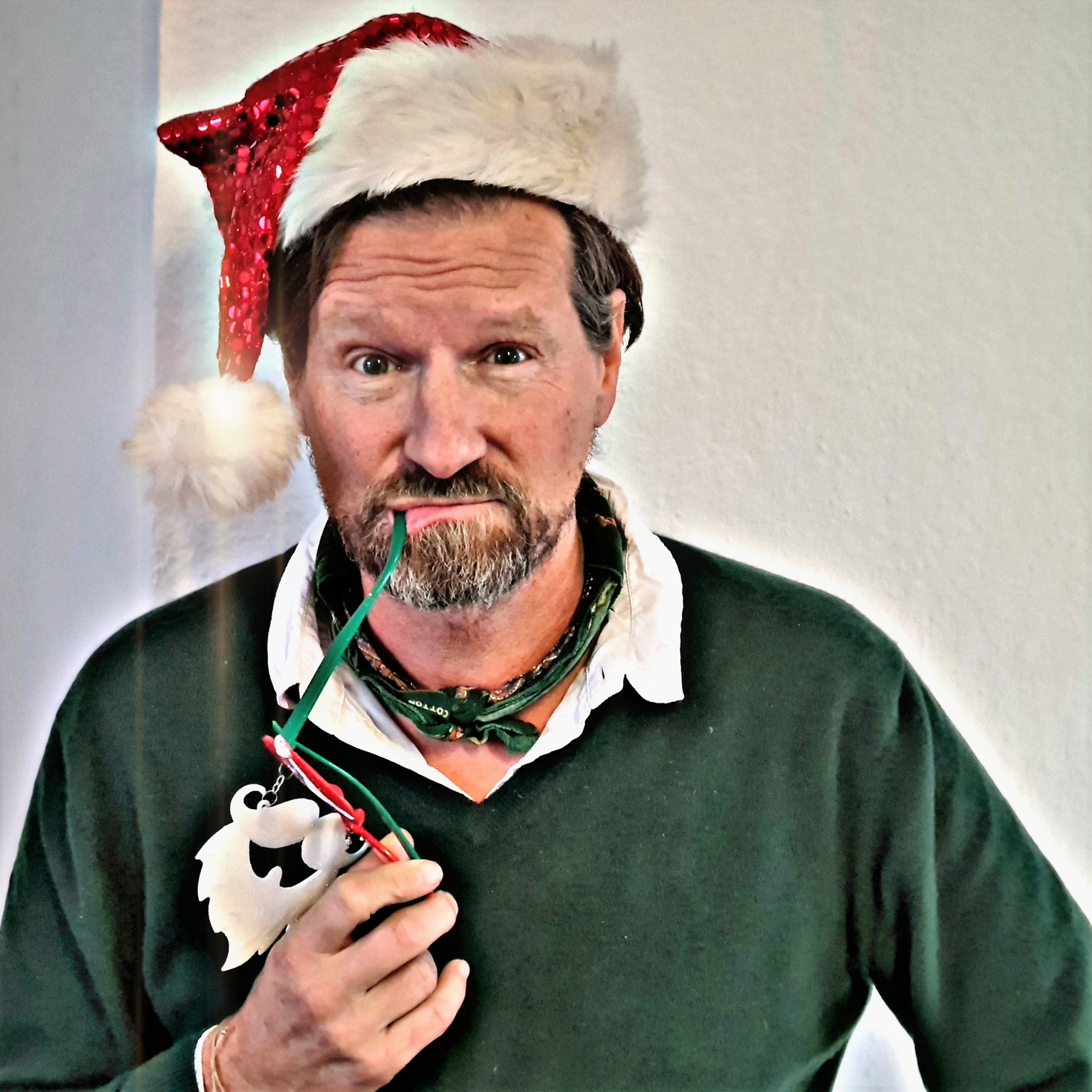 Mann mit Weihnachtsmütze, der den Bügel seiner Deko-Brille wie eine Pfeife im Mund trägt