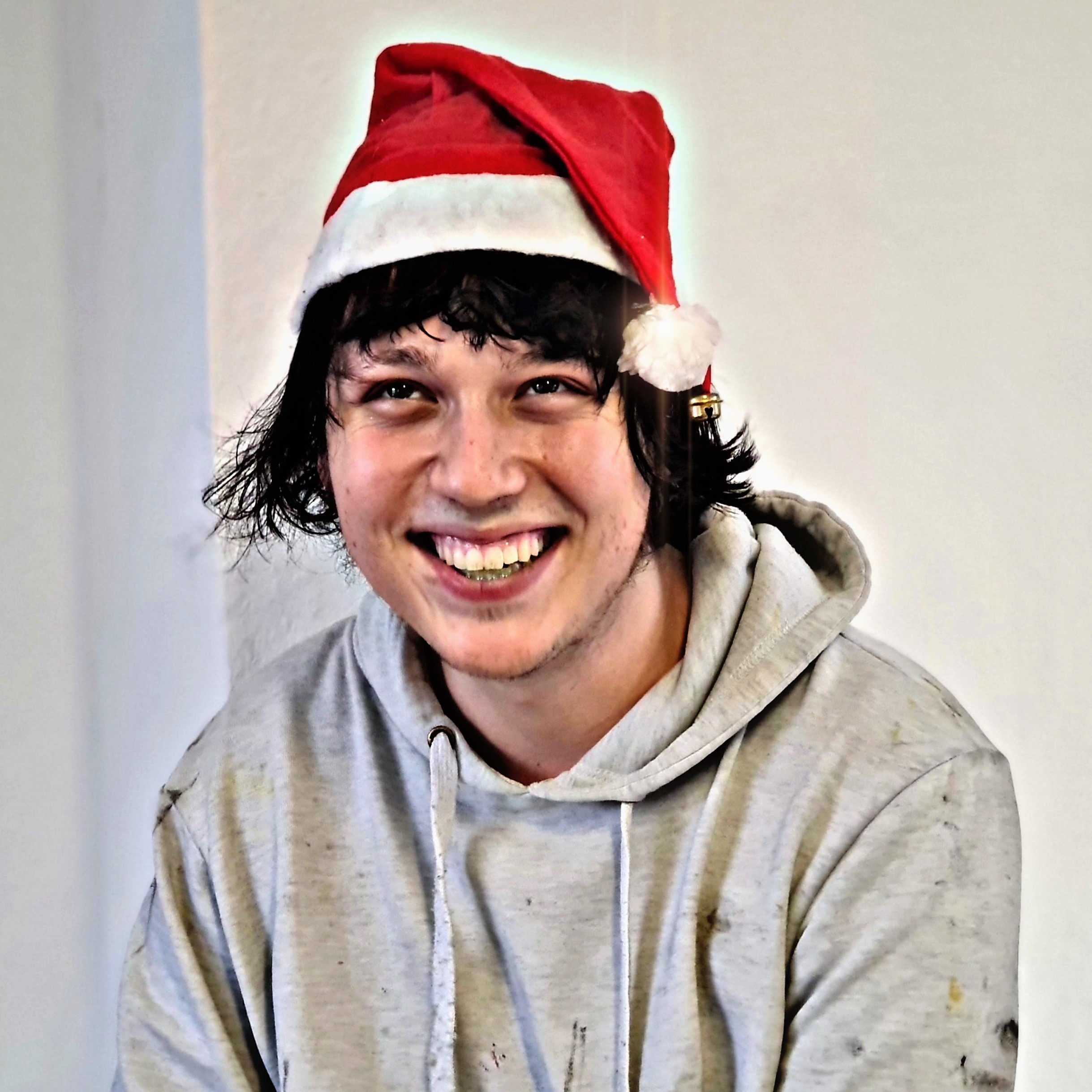 Junger Mann mit roter Zipfelmütze und grauem Hoodie lacht in die Kamera