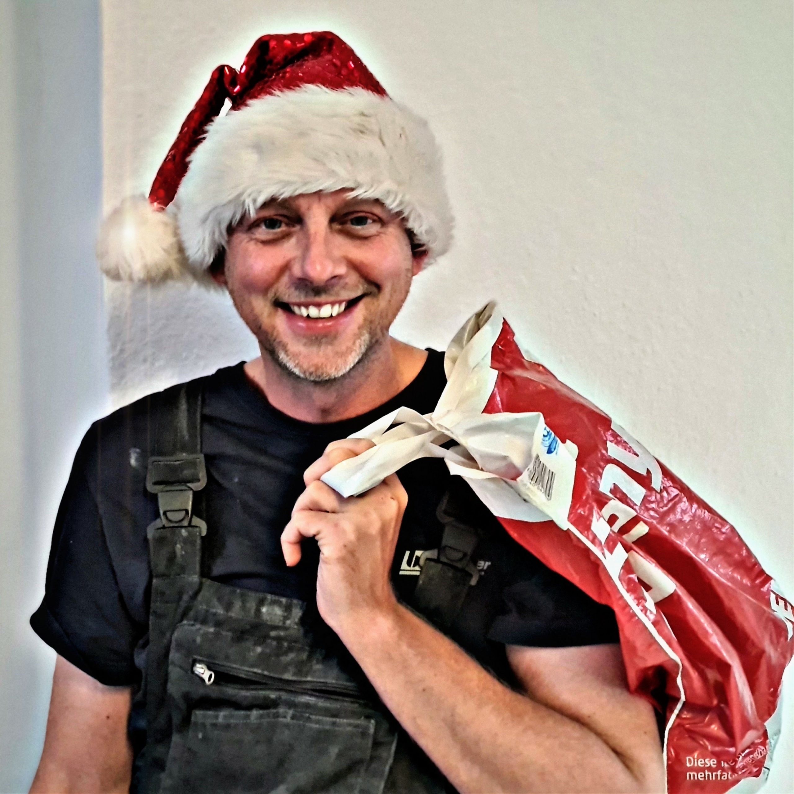 Mann mit roter Weihnachtsmütze und Tüte über der Schulter, fröhlich grinsend