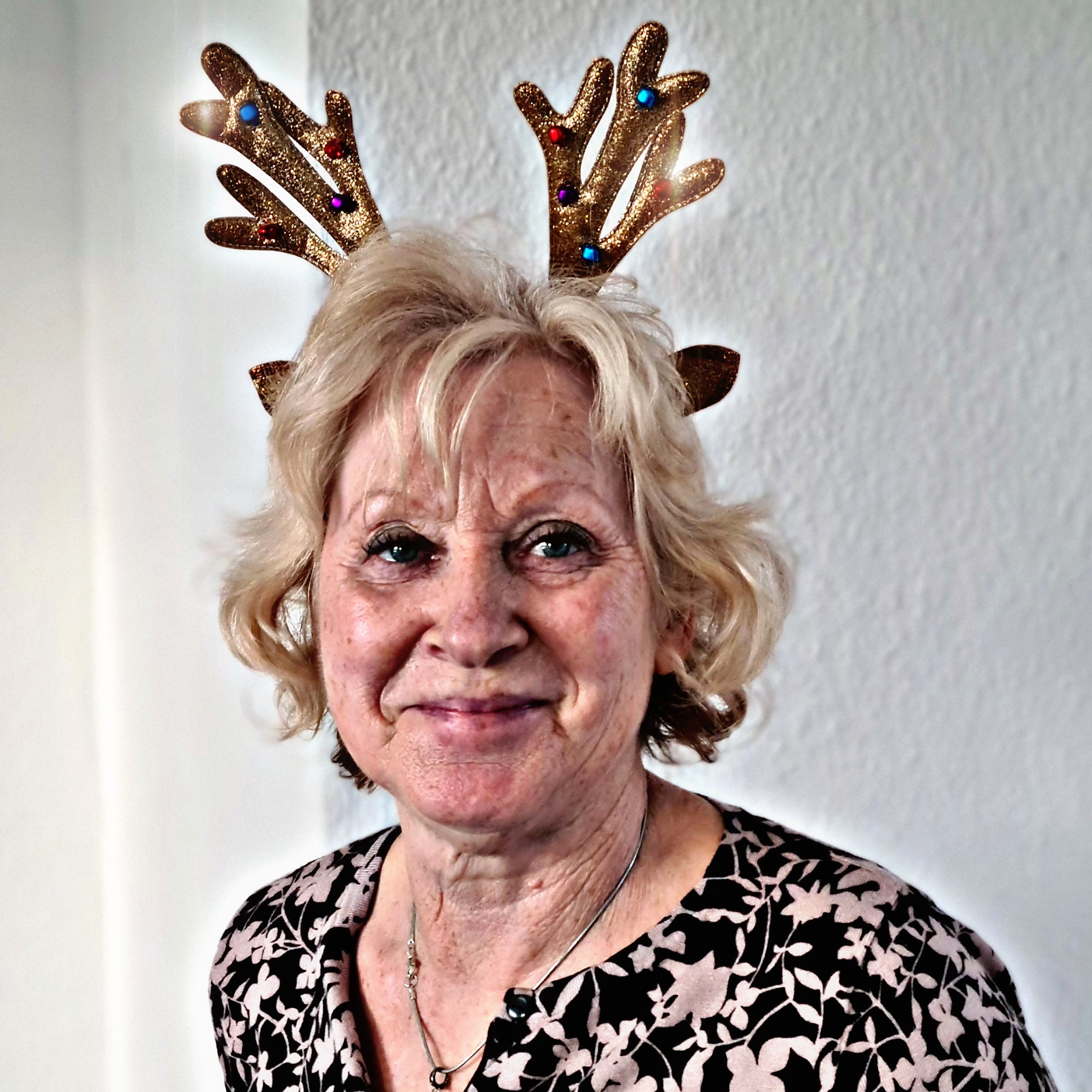 Ältere Frau mit glitzerndem Rentiergeweih-Haarreif und Blumenbluse