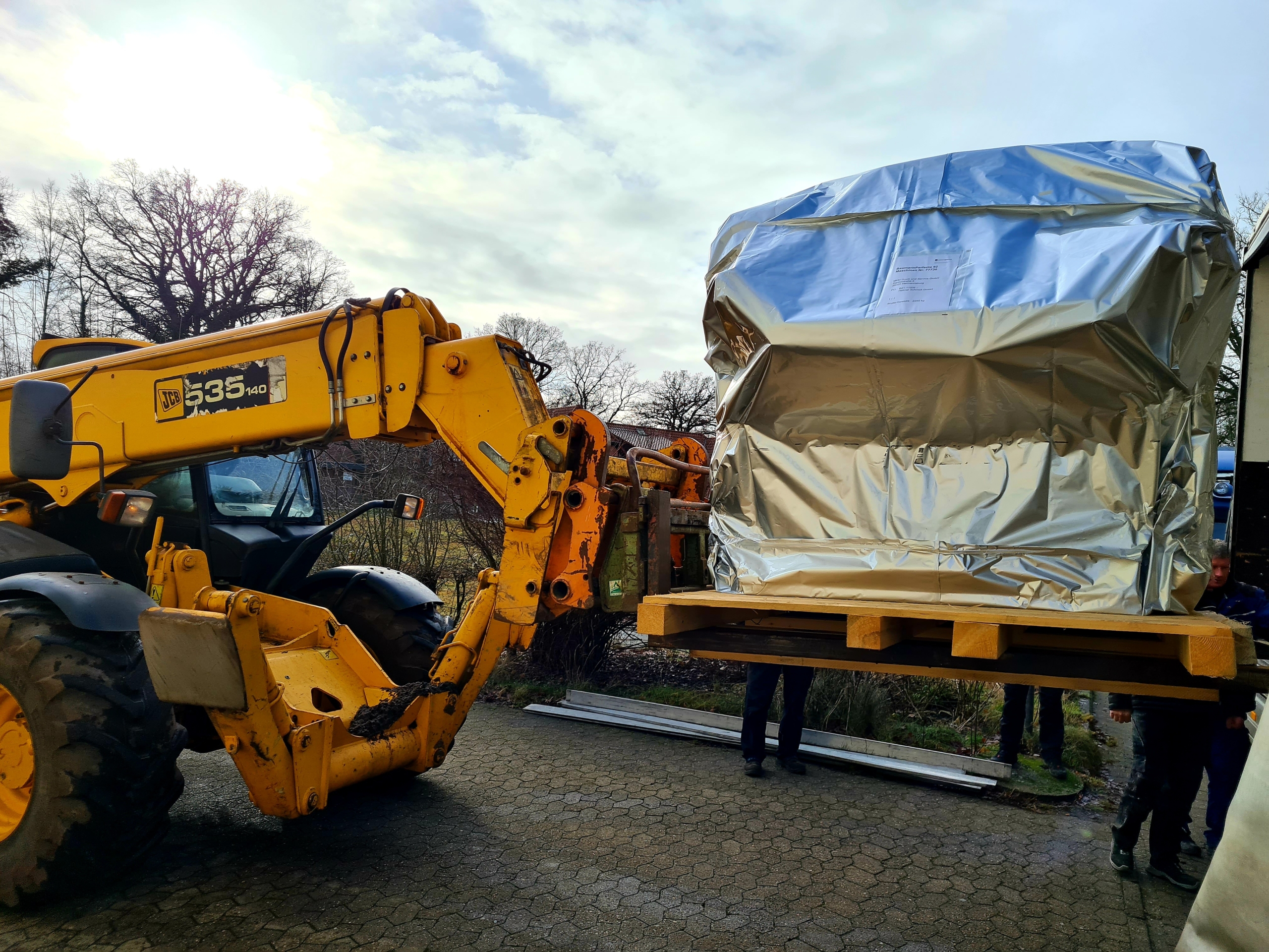 Gelber Teleskoplader hebt verpackte Schneidemaschine auf Holzpalette an