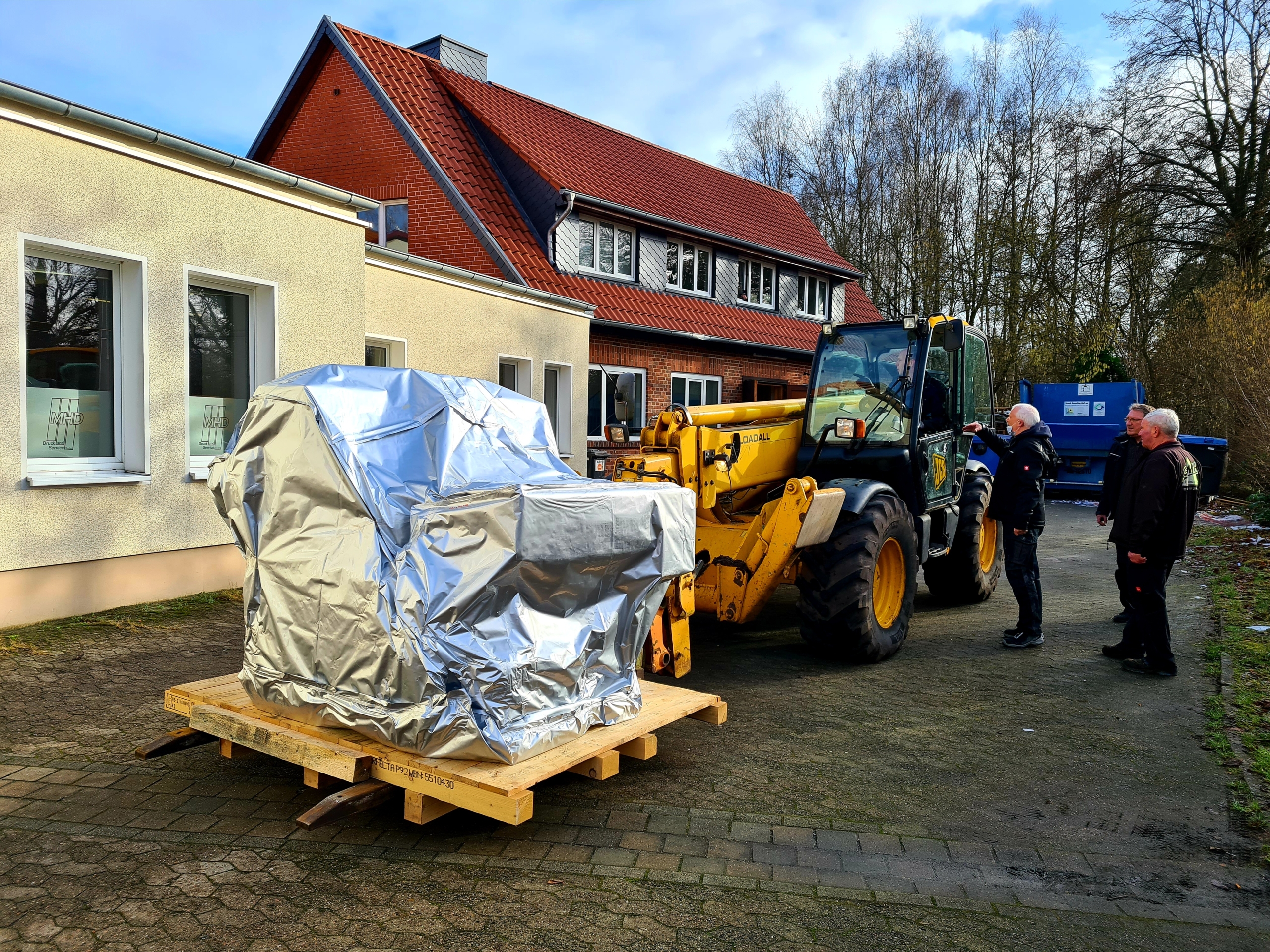 Maschine vor dem MHD-Gebäude mit Teleskoplader und drei Personen