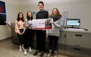 Vier Personen präsentieren einen Druckbogen in einem Produktionsraum mit Großdrucker