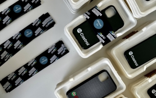 Nachhaltige Handyhüllen und Bänder mit Castrol-Logo in Verpackung auf weißem Tisch
